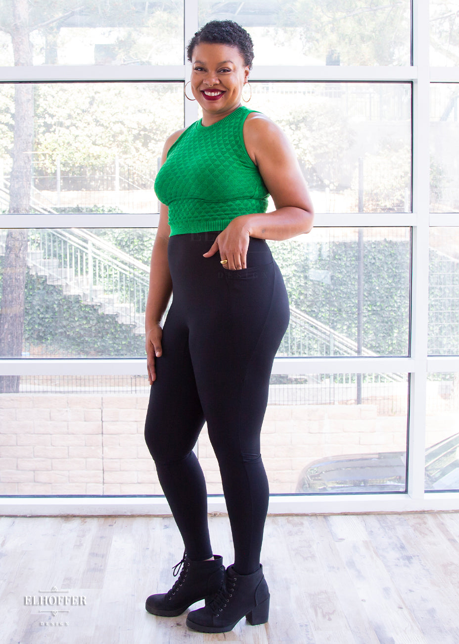 Desiree, a size large medium dark skinned model with very short dark hair, is wearing a pair of high waisted black leggings with a seamless front and side seam pockets in black.