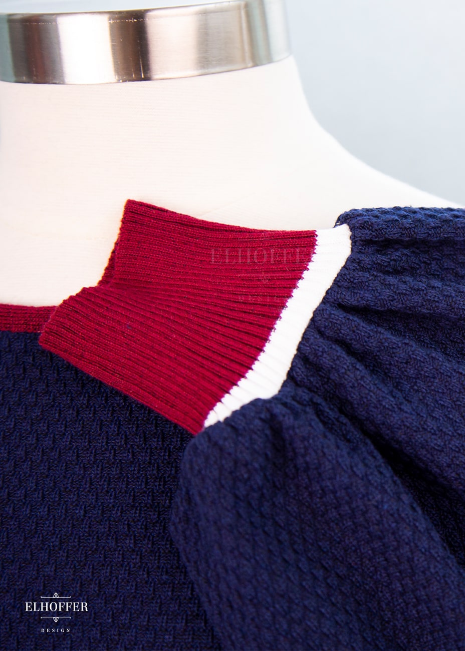 Close up of red cuff with white stripe detailing and blue waffle knit texture of sleeve.
