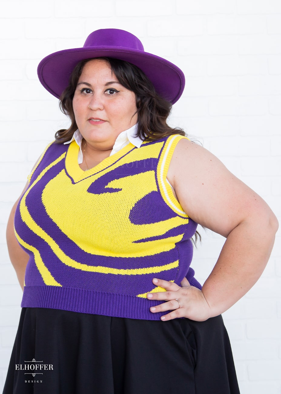Alysia, a fair skinned, size XL model with dark brown hair, is wearing a pullover vest with a boxy fit and v-neck. It is bright purple with a yellow swirl detail across the body.