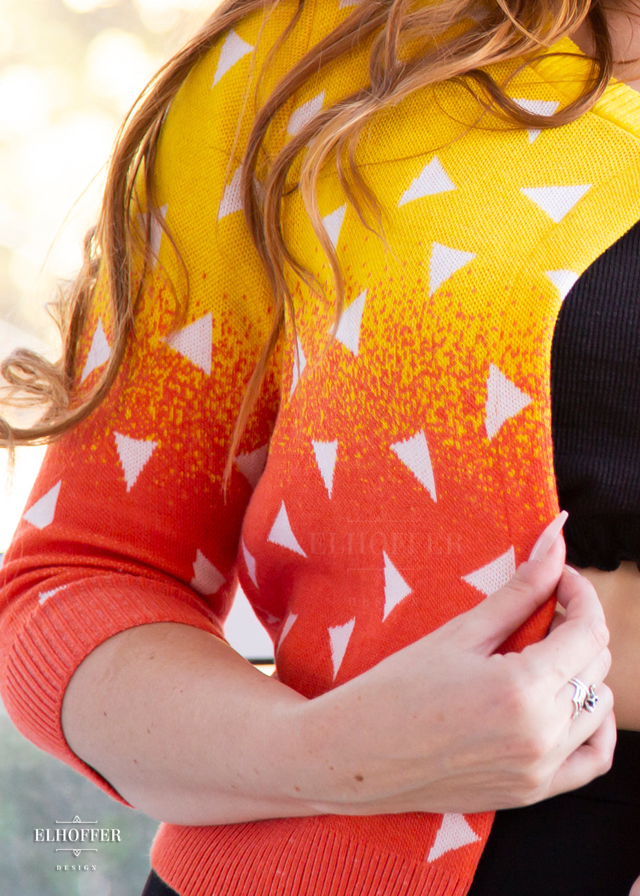 A close up of the yellow to orange gradient knit pattern with white triangles throughout.