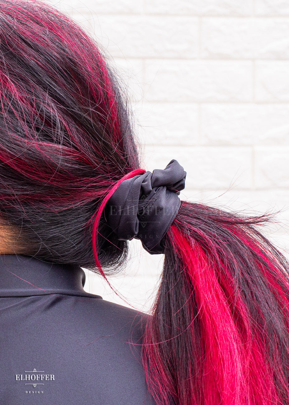 A solid black scrunchie holding bright pink and black hair in a ponytail.