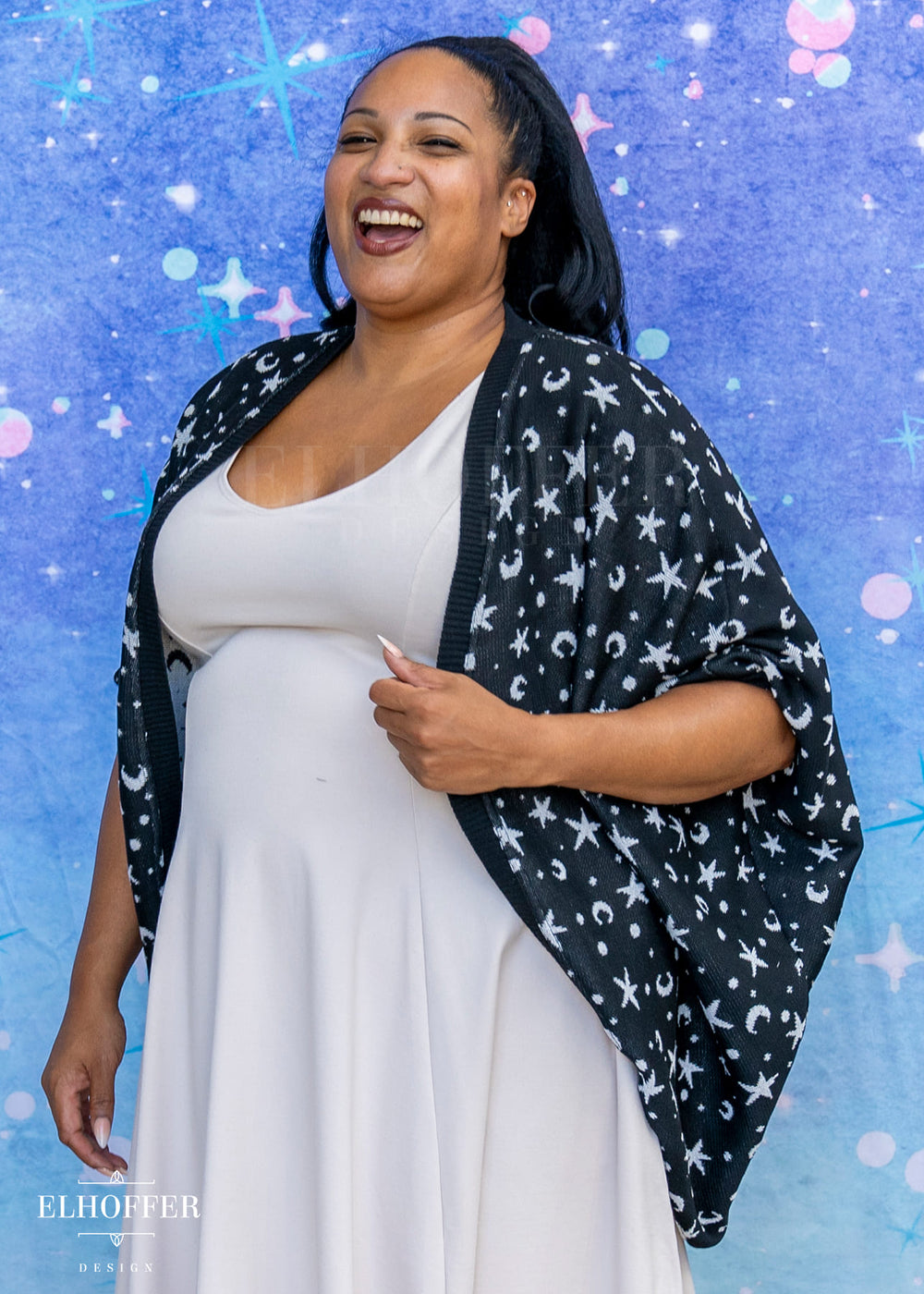 Woman wearing a white dress with a black star-patterned shawl against a blue background