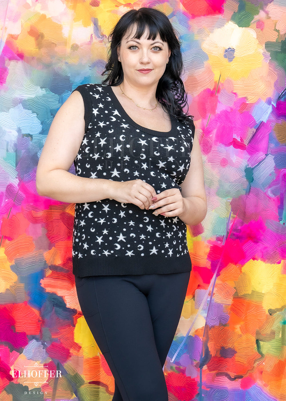 Woman wearing a black sleeveless top with white patterns against a colorful abstract background