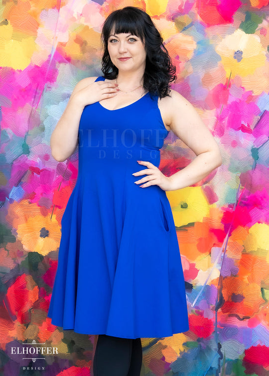 Woman wearing a blue dress against a colorful floral background with 'Elhoffer Designs' branding.