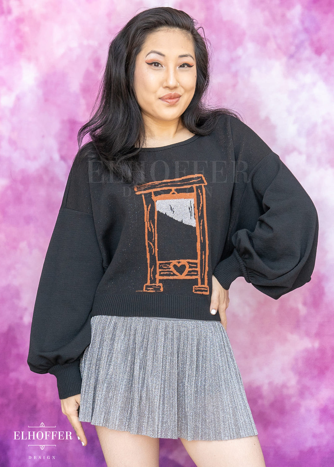 Woman wearing a black sweater with a design and gray skirt against a pink and purple gradient background