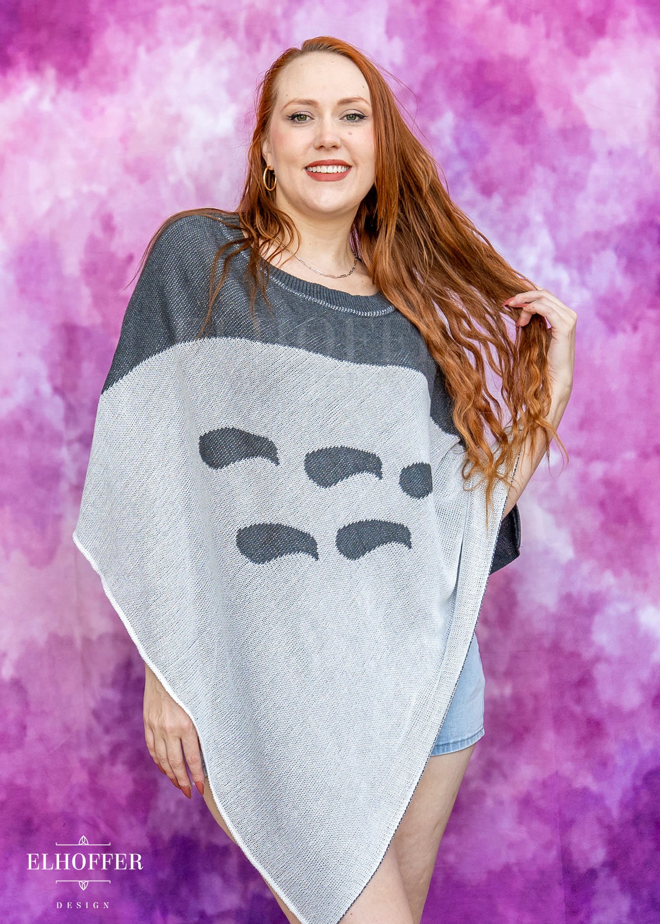 Woman wearing a poncho with a face design against a pink and purple gradient background