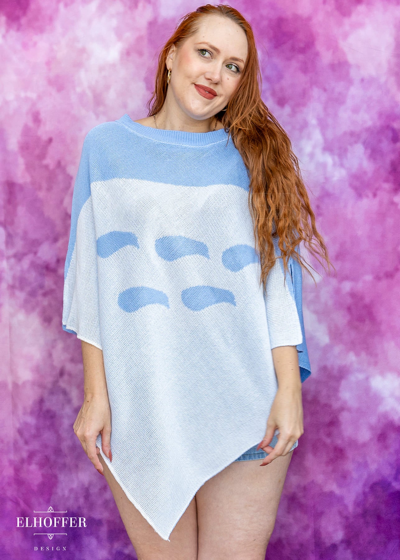 Woman wearing a blue and white sweater with abstract designs against a pink and purple gradient background.