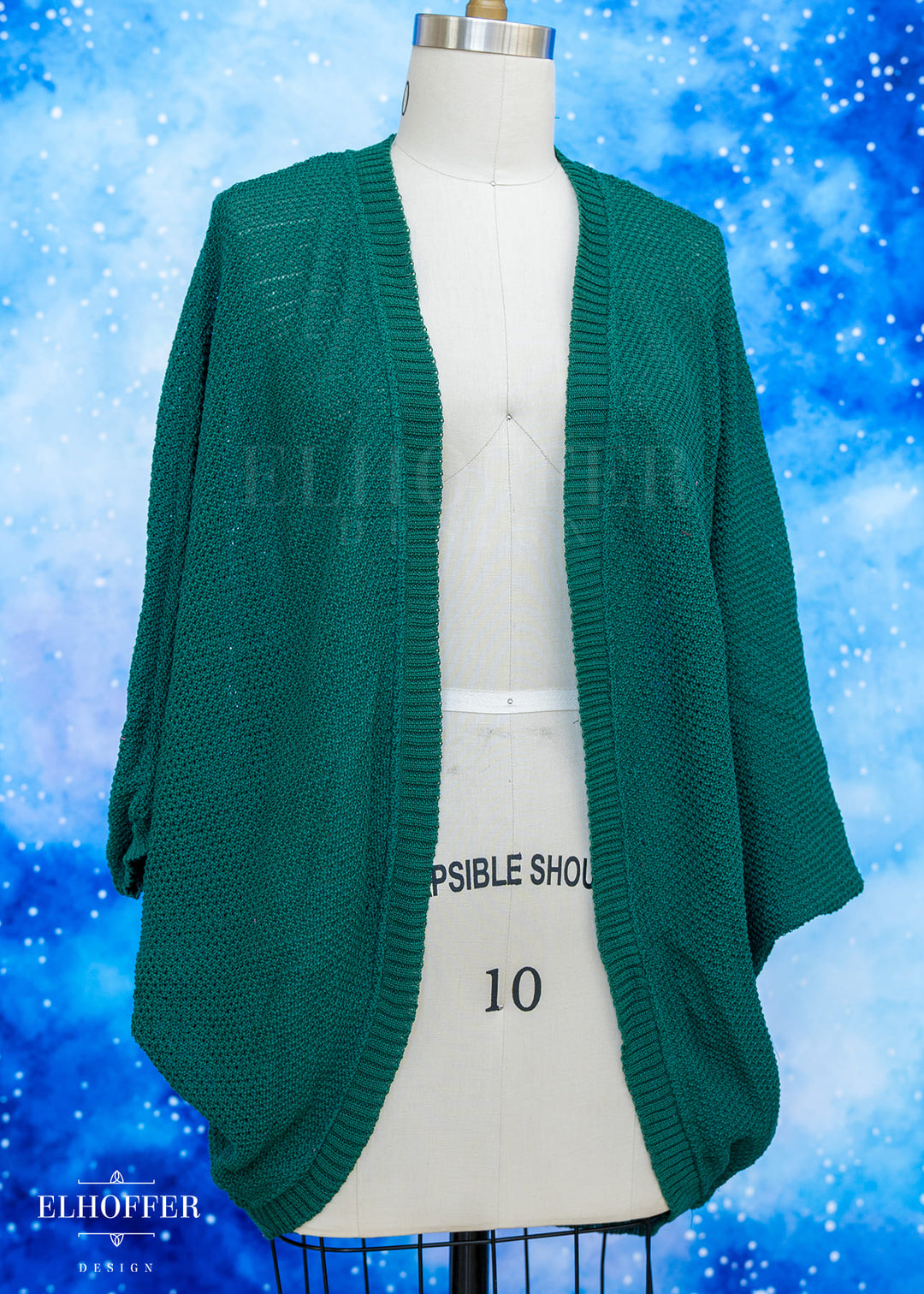 Green cardigan on a mannequin against a blue snowy background with 'Elhoffer' branding.