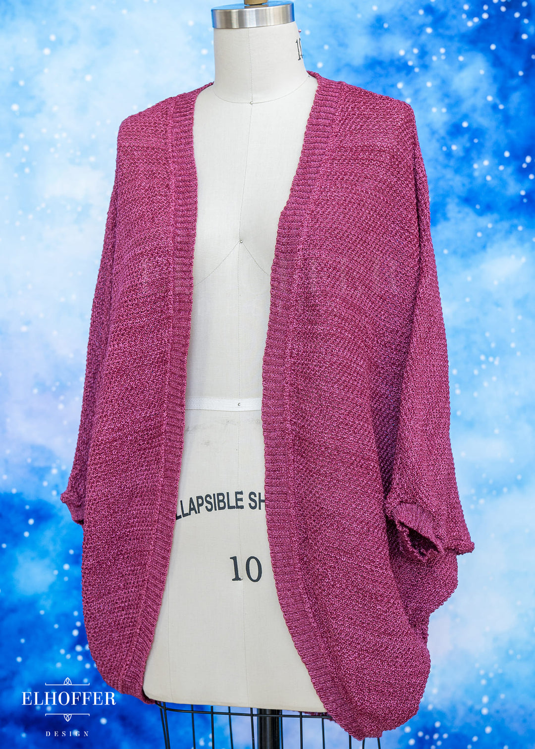 Pink cardigan on a mannequin against a blue snowy background with 'Elhoffer' branding.
