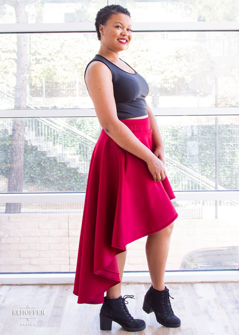 Desiree, a size large medium dark skinned model with very short dark hair, is wearing a burgundy commander skirt and black tank. The commander skirt is a high waisted hi-low skirt that stands away from the body due to the double scuba fabric with encased elastic waistband with matching lining.