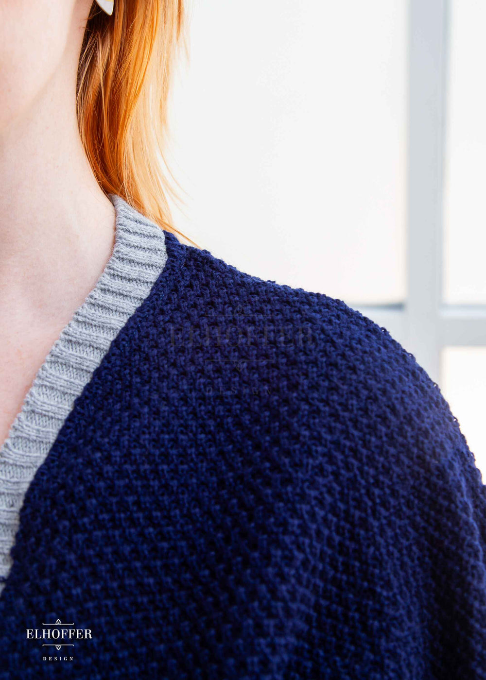 Close up of blue loose knit weave and light grey ribbing along neckline.