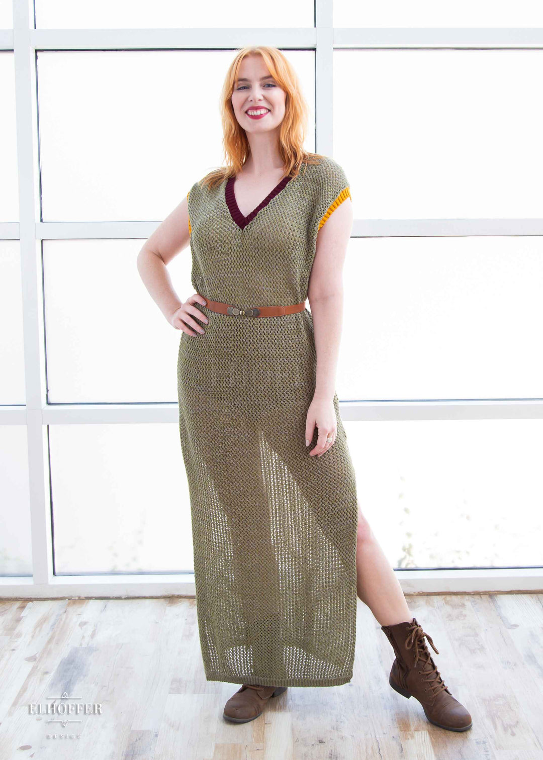 Harley, a fair skinned S model with shoulder length strawberry blonde hair, is wearing a long reversible sleeveless loose knit cover up with side slits.  The main body is an olive green with one side plain knit with a v neck and the other side having a subtle skull design with a scoop neck, the neckline is trimmed in crimson red, and the armholes are trimmed in a yellow.