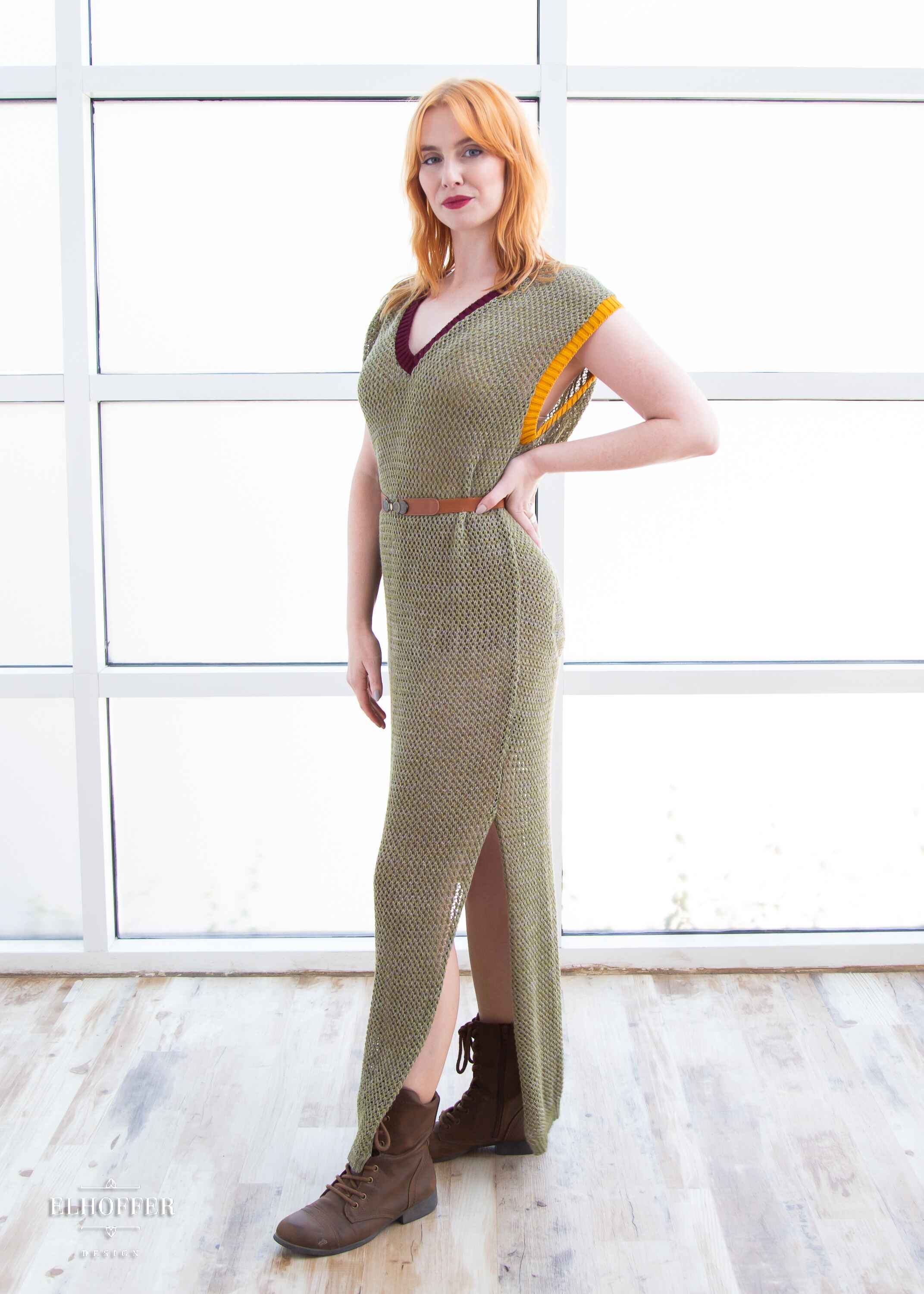 Harley, a fair skinned S model with shoulder length strawberry blonde hair, is wearing a long reversible sleeveless loose knit cover up with side slits.  The main body is an olive green with one side plain knit with a v neck and the other side having a subtle skull design with a scoop neck, the neckline is trimmed in crimson red, and the armholes are trimmed in a yellow.