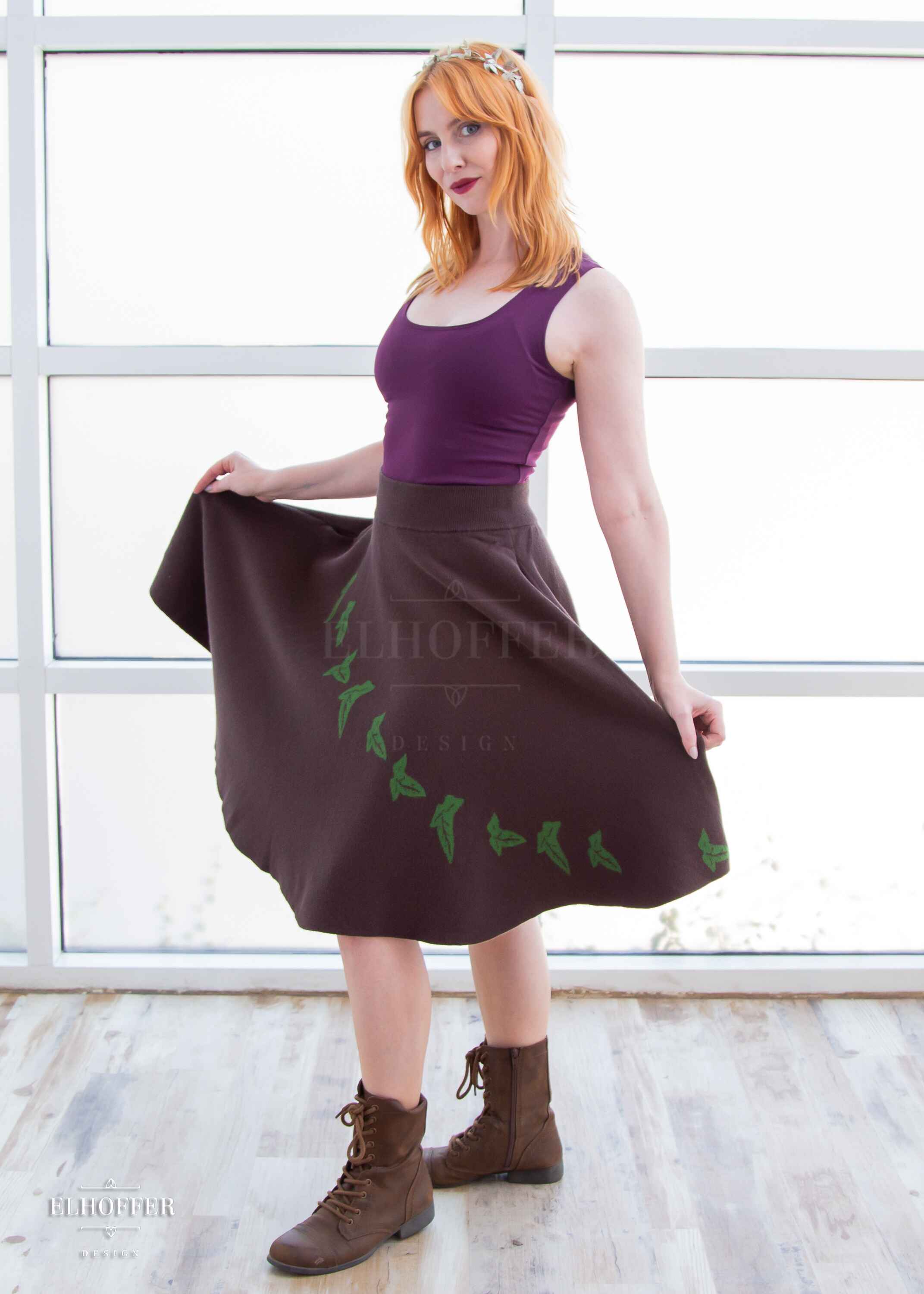 Harley, a fair skinned S model with shoulder length strawberry blonde hair, is wearing a brown knit skirt that hits just passed the knee and has a cascading green leaf design and a dark purple scoop necked crop top.