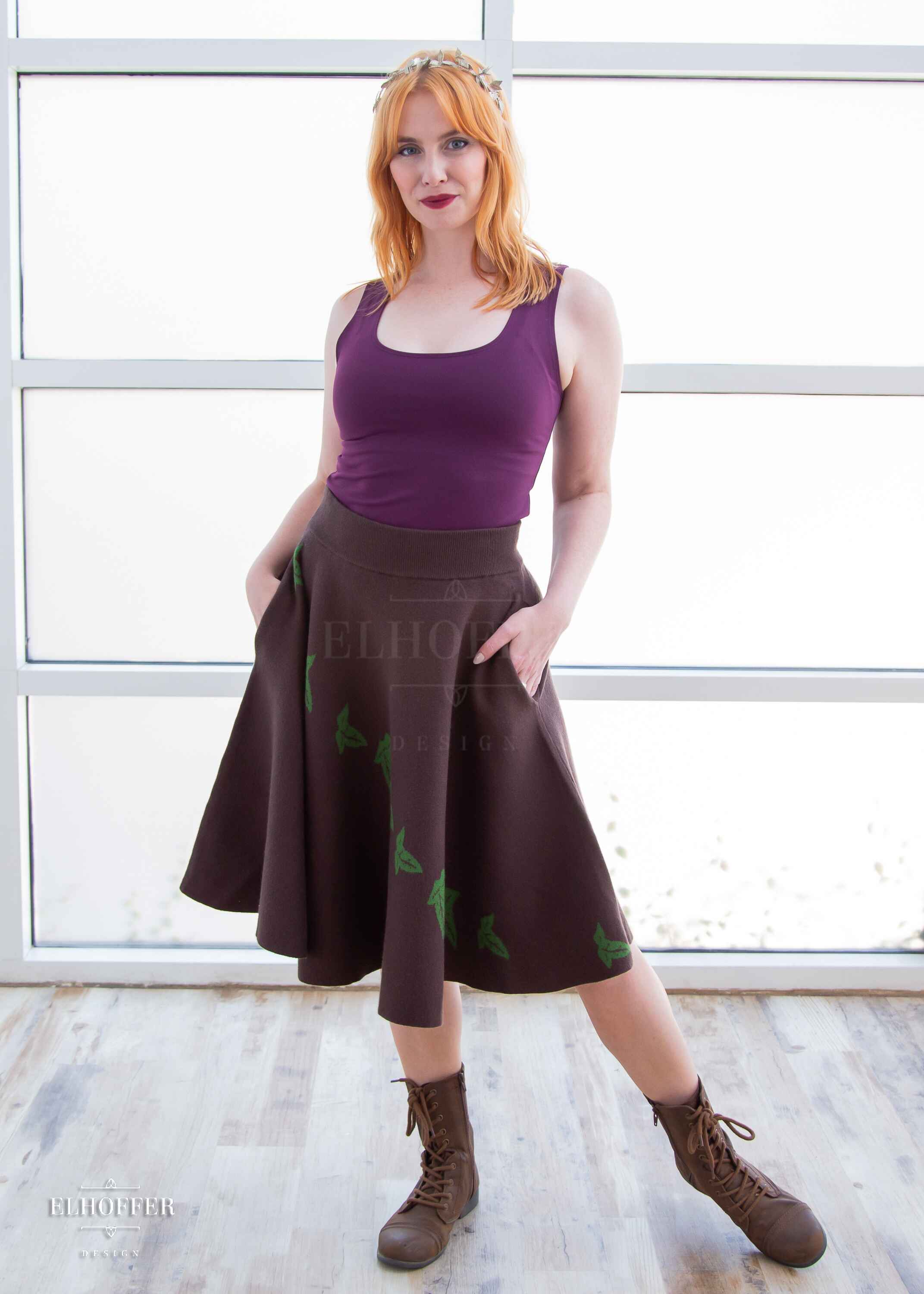 Harley, a fair skinned S model with shoulder length strawberry blonde hair, is wearing a brown knit skirt that hits just passed the knee and has a cascading green leaf design and a dark purple scoop necked crop top.