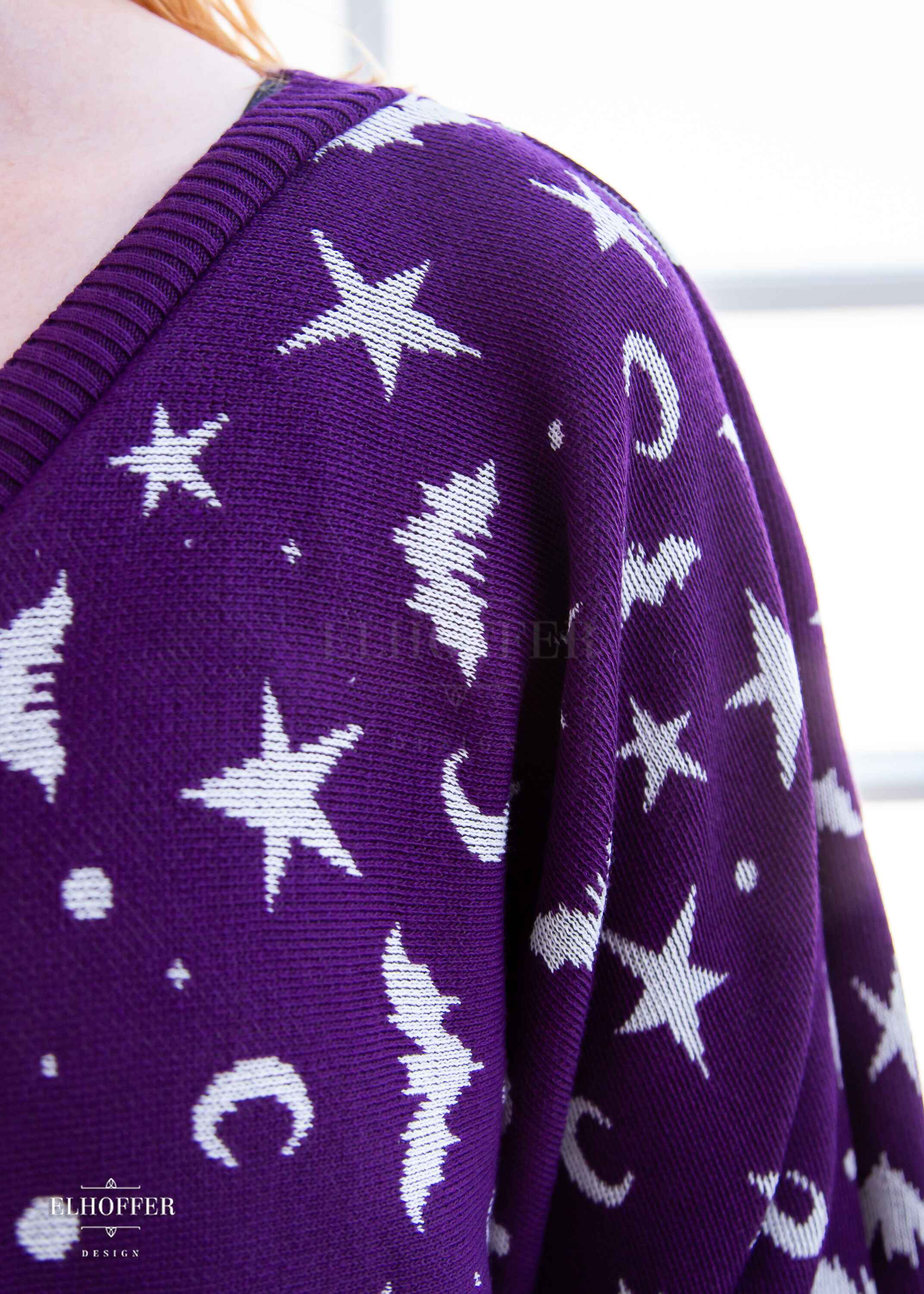 A closeup of the white bat and moon pattern in the purple knit sweater