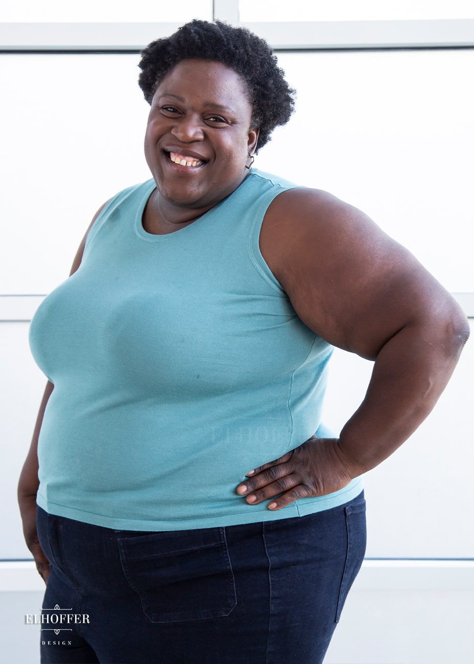 Adalgiza, a dark skinned size 4XL model with short curly black hair, is wearing our pullover sleeveless sweater tank in seafoam blue.