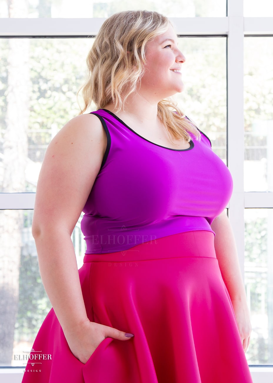 Sarah, a fair skinned size XL model with long blonde hair, wears a low scoop neckline sleeveless crop top with black foldover binding at the neck and armholes, wide shoulder straps, fitted throughout the body, and ending at the natural waist in a bright magenta.