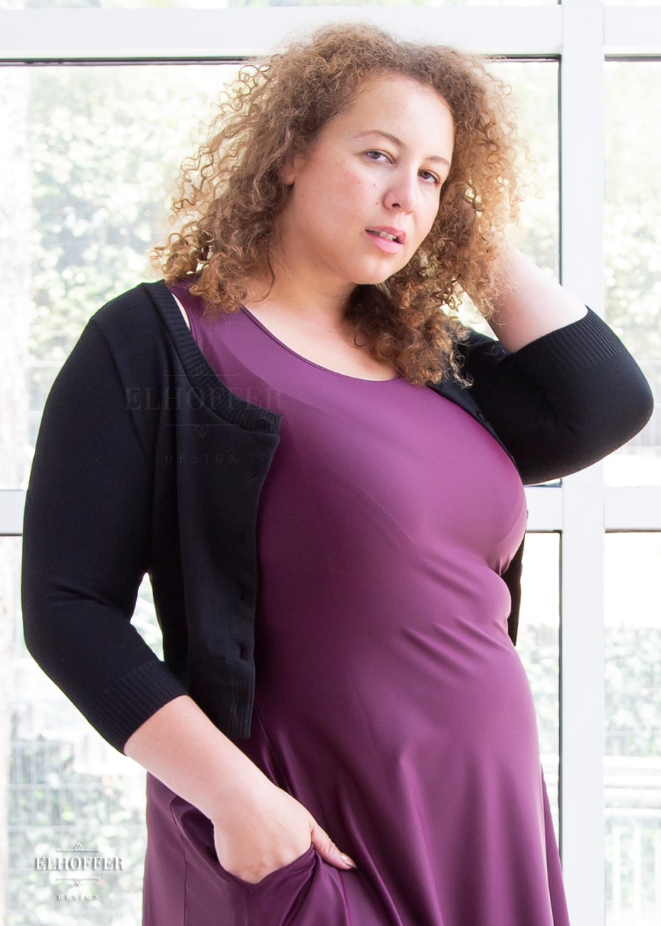 Anastasia, a curly haired, medium-skinned size XL model, is wearing our essential Cordelia cropped cardigan in black. It is a button front cropped cardigan with long sleeves and a scooped neck.