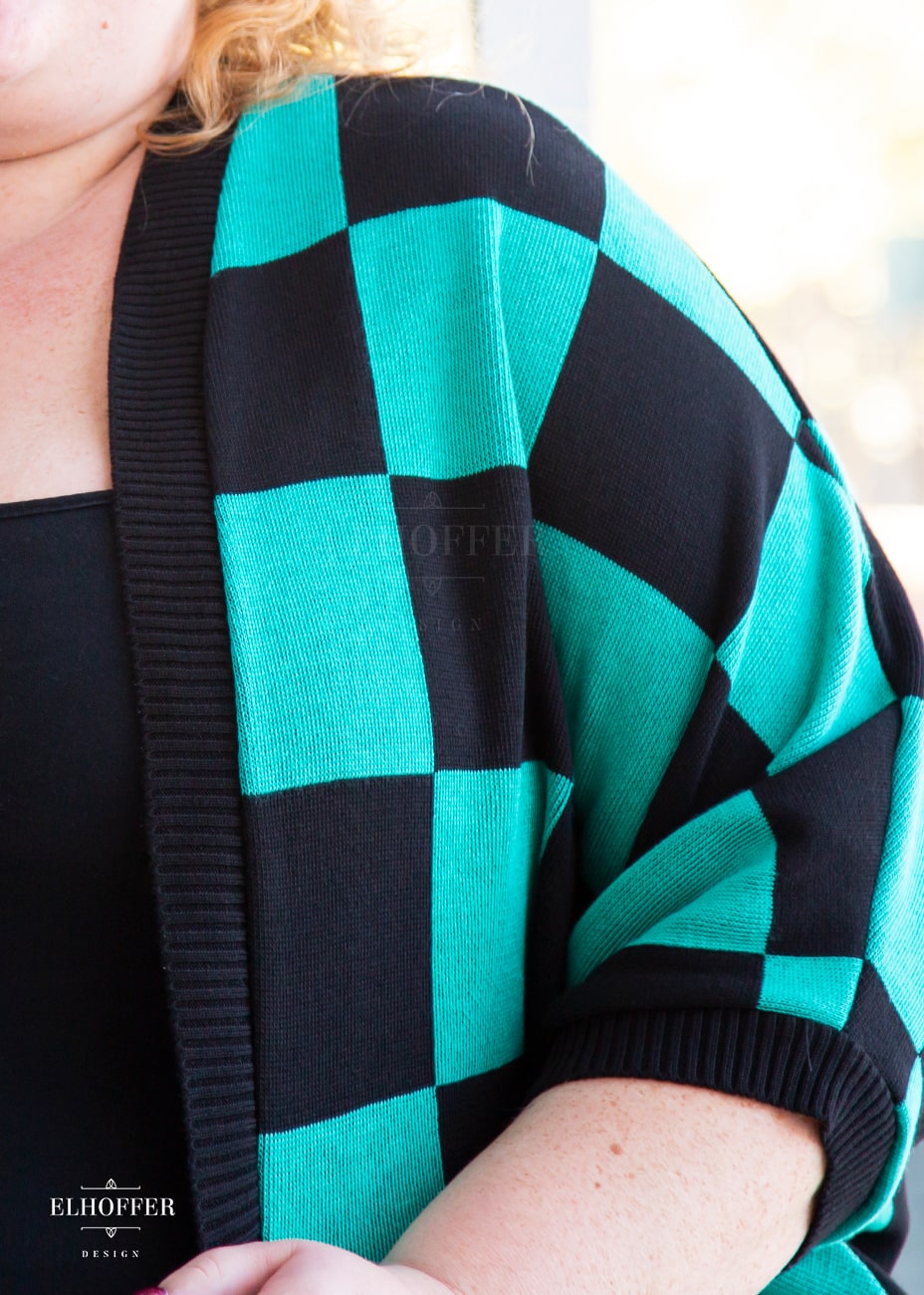 Close up of the black and green chessboard knit pattern and black ribbing around front and cuff.
