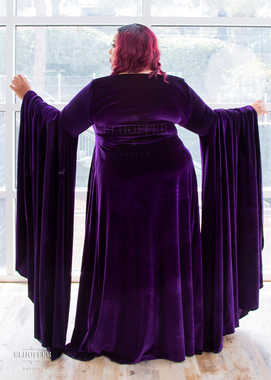 Dawn models the back of the full length purple velvet dress. The sleeves are fitted to the elbow and are full and the ends fall to the floor.