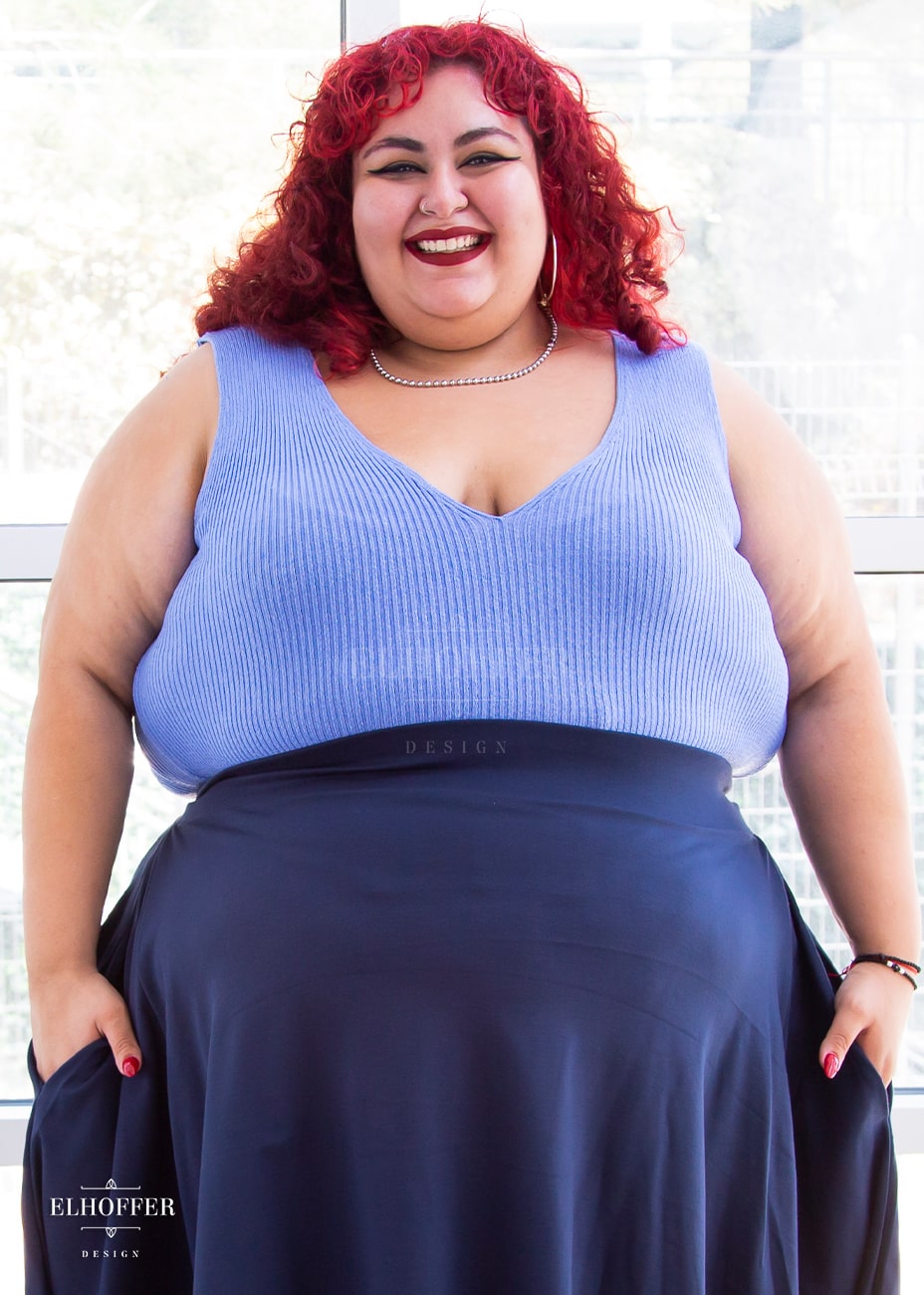 Victoria, an olive skinned size 4XL model with bright red curly hair, is wearing a pullover sleeveless ribbed v-neck tank in light blue. The v-neck is actually reversible and offers two depths.