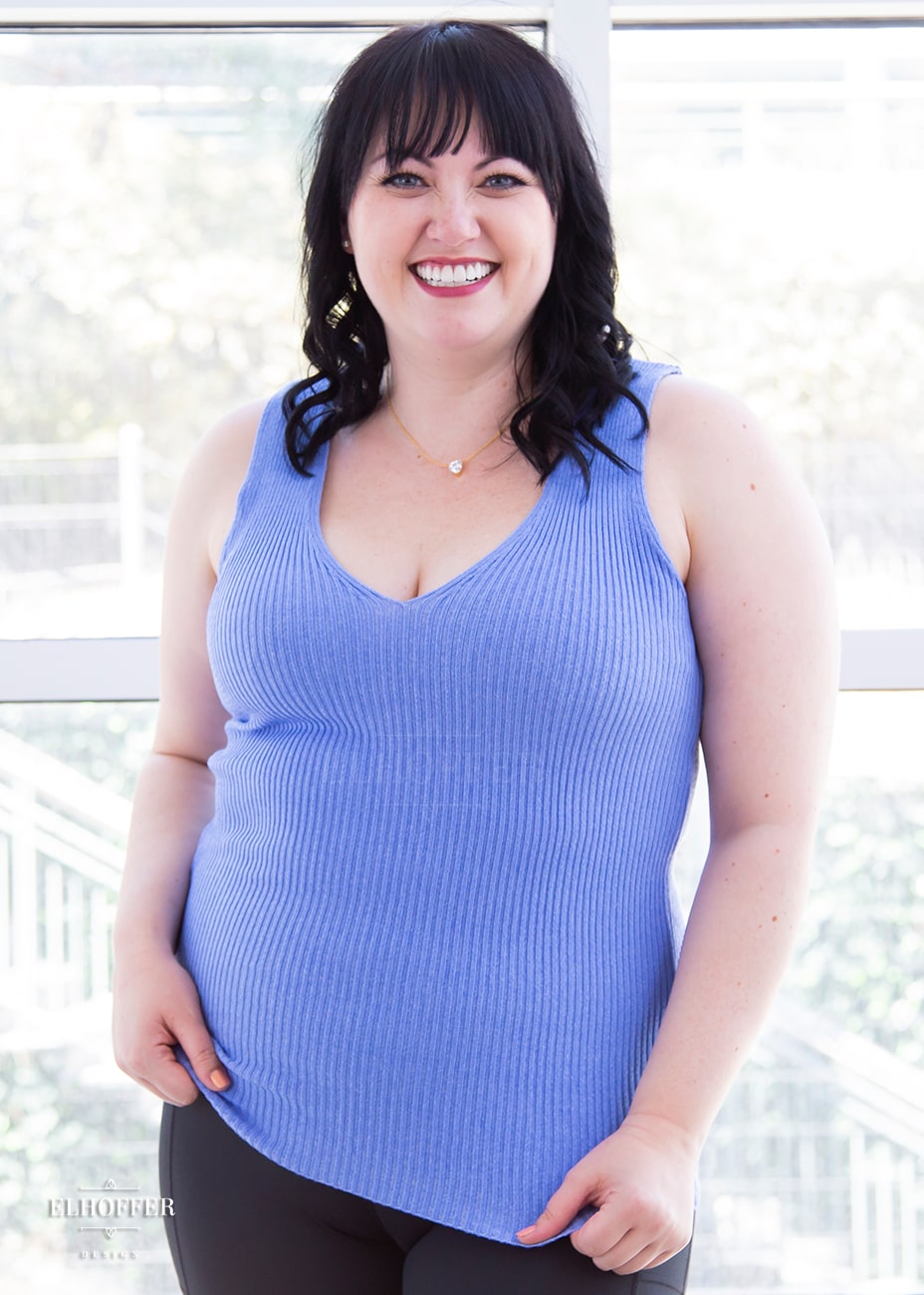 Bernadette, a fair skinned size large model with short black hair and bangs, is wearing a pullover sleeveless ribbed v-neck tank in light blue. The v-neck is actually reversible and offers two depths.