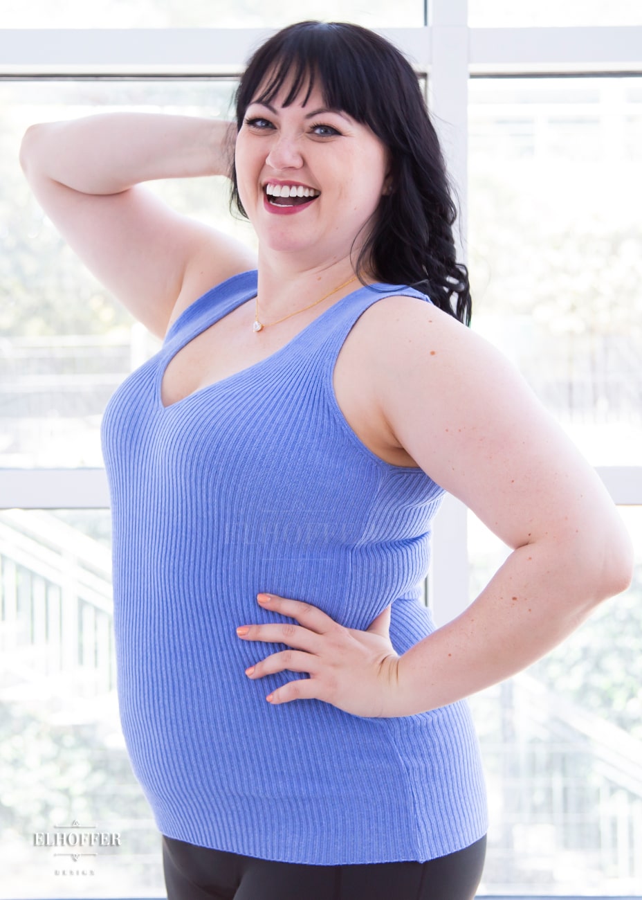 Bernadette, a fair skinned size large model with short black hair and bangs, is wearing a pullover sleeveless ribbed v-neck tank in light blue. The v-neck is actually reversible and offers two depths.