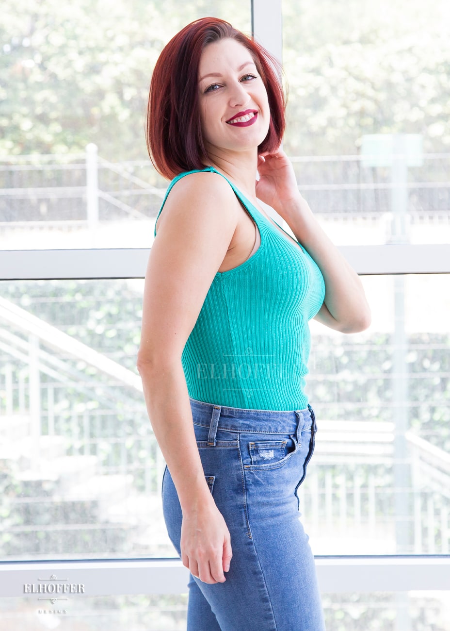 Natalie, a size small fair skinned model with short red hair, is wearing our essential gemini tank in poison green, a light teal. The pullover sleeveless knit tank is meant to be reversible with a shorter and longer V-Neck you can decide how low to go.