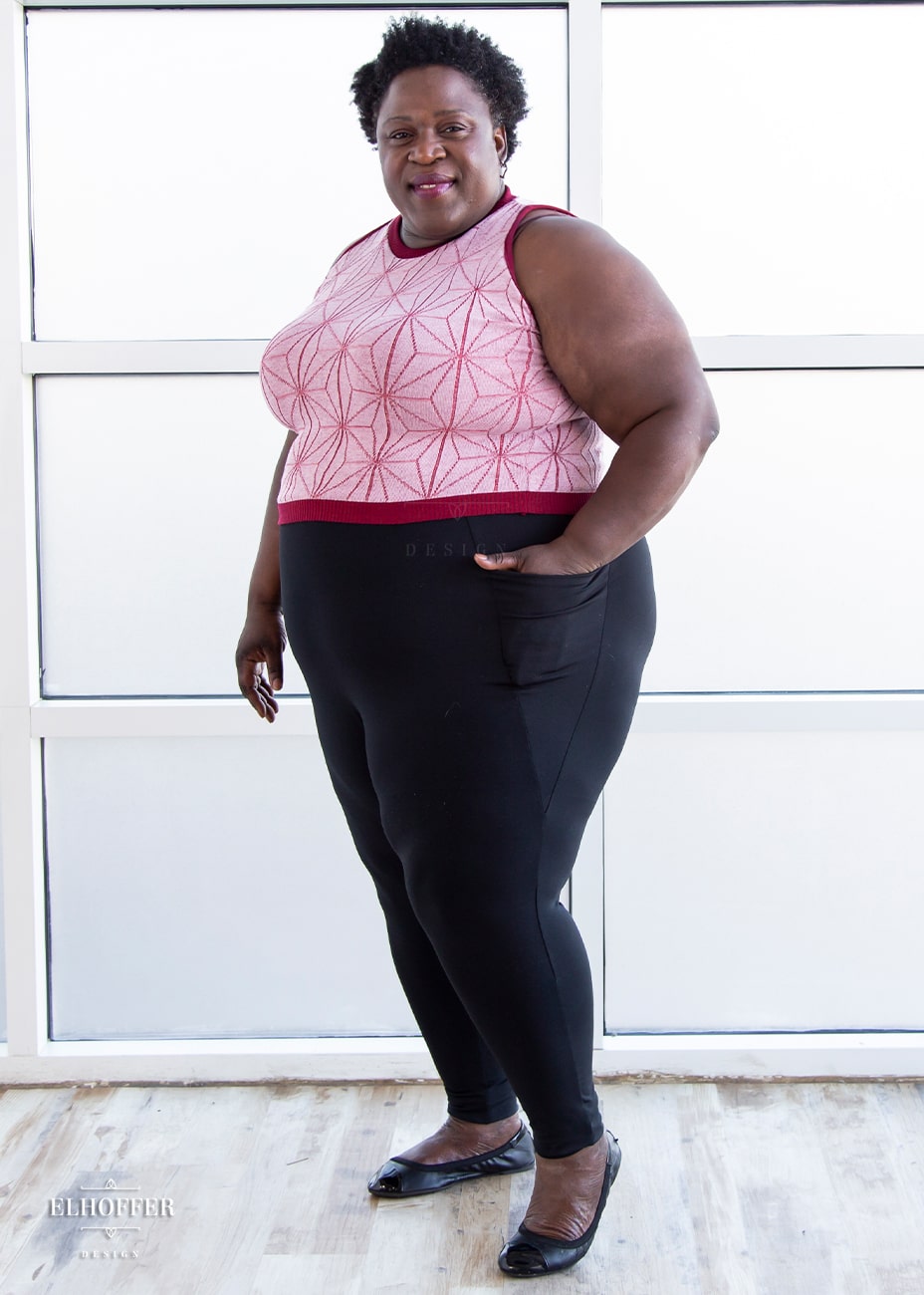 Adalgiza, a dark skinned 4XL model with short curly hair, is wearing a pair of high waisted black leggings with a seamless front and side seam pockets in black.