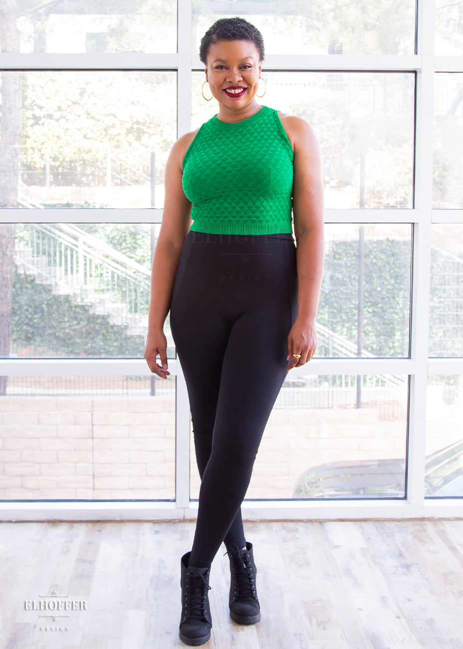 Desiree, a size large medium dark skinned model with very short dark hair, is wearing a pair of high waisted black leggings with a seamless front and side seam pockets in black.
