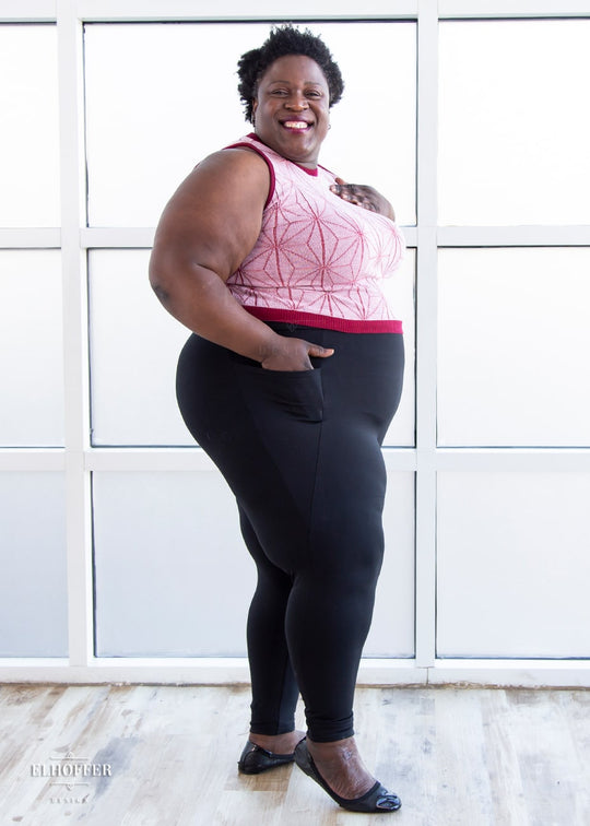 Adalgiza, a dark skinned 4XL model with short curly hair, is wearing a pair of high waisted black leggings with a seamless front and side seam pockets in black.