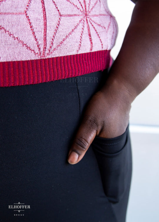 Adalgiza, a dark skinned 4XL model with short curly hair, is wearing a pair of high waisted black leggings with a seamless front and side seam pockets in black.