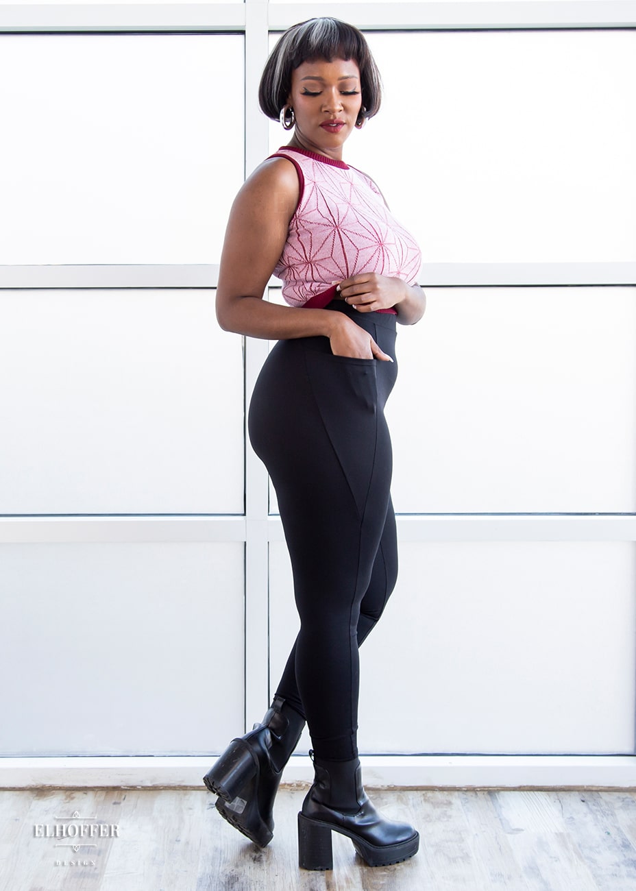 Lynsi, a medium dark skinned model with short dark brown hair with white highlights, is wearing a pair of high waisted leggings with a seamless front and side seam pockets in black.