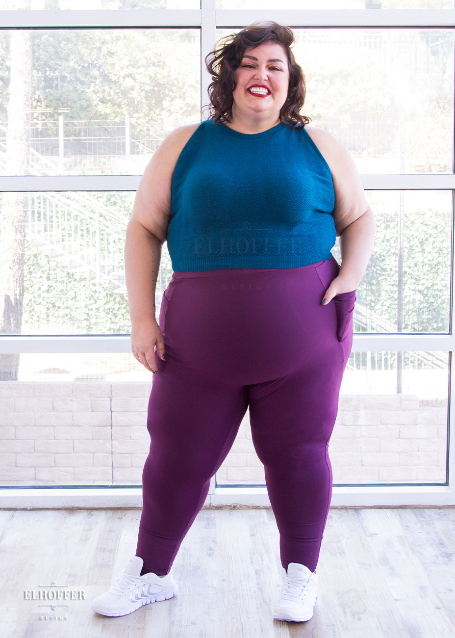 Kristen, a size 3XL olive skinned model with short dark brown hair, is wearing a pair of high waisted leggings with a seamless front and side seam pockets in plum.
