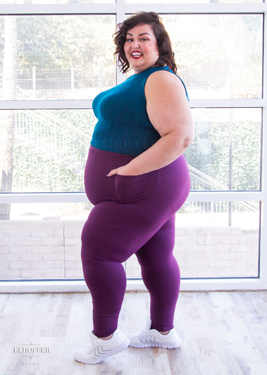 Kristen, a size 3XL olive skinned model with short dark brown hair, is wearing a pair of high waisted leggings with a seamless front and side seam pockets in plum.