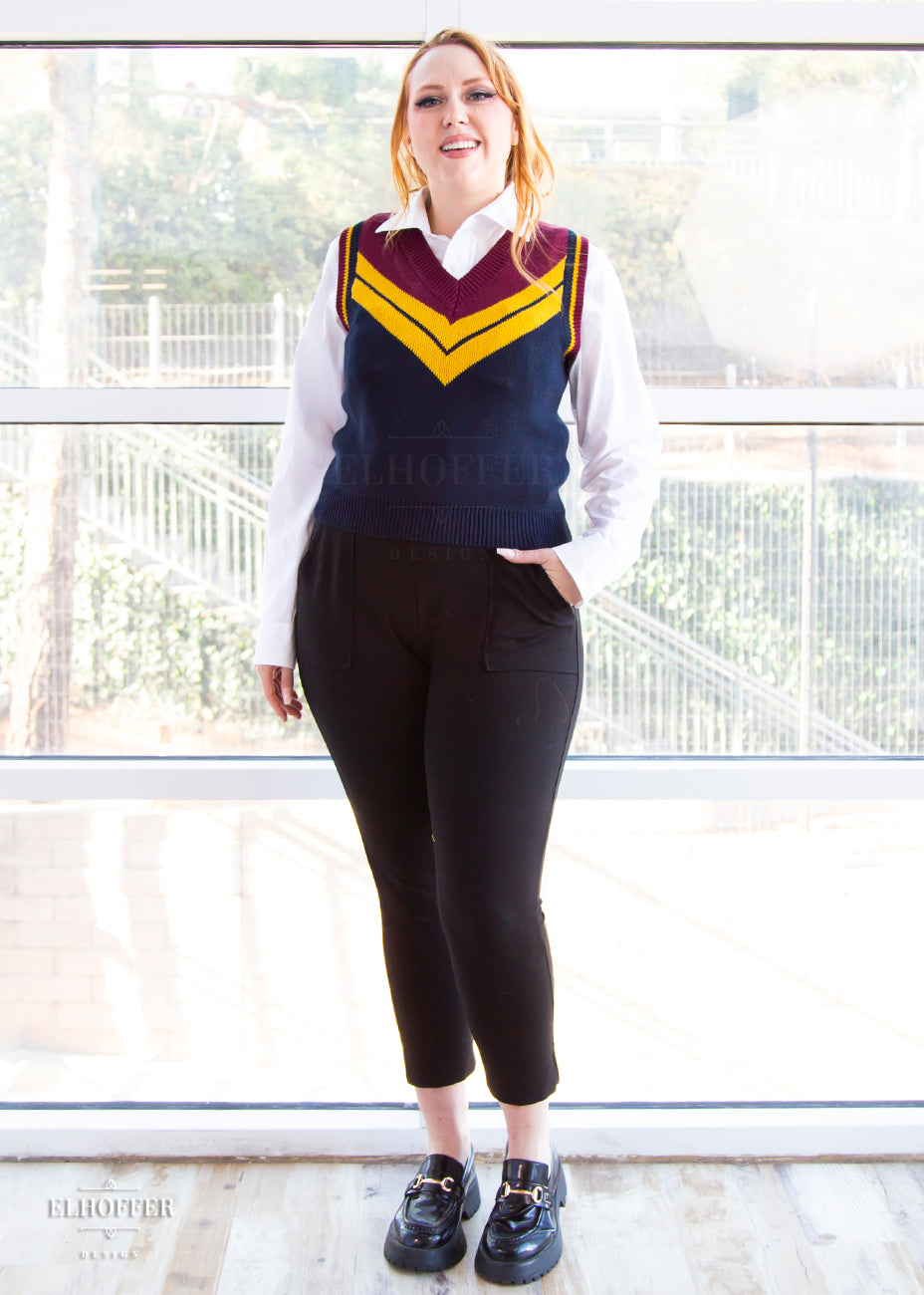 Kelsey, a size small model with long ginger hair, is wearing a pullover vest with a boxy fit and v-neck. It is navy blue with a deep red neckline and mustard yellow v detail.