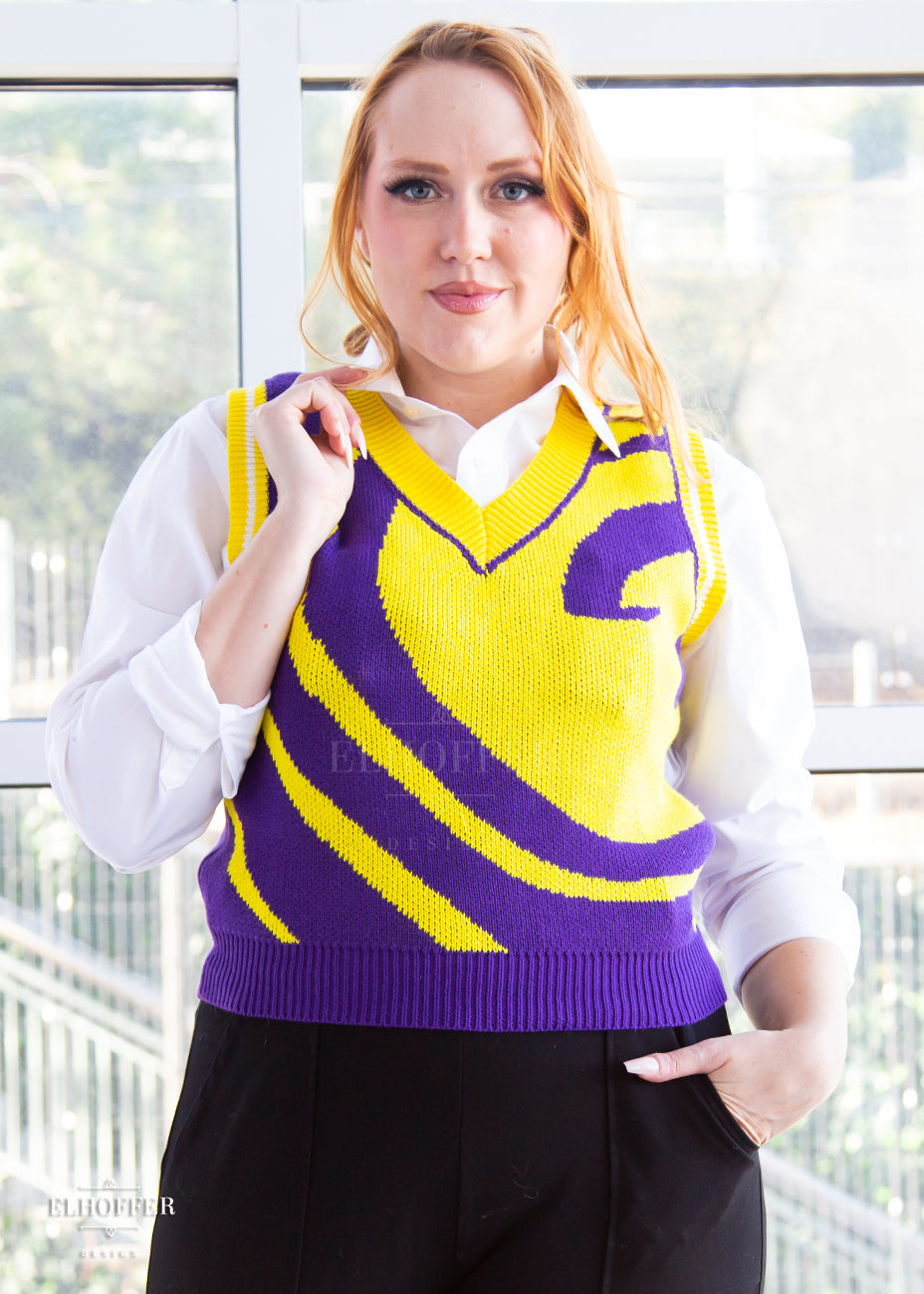 Kelsey, a size small fair skinned model with long ginger hair, is wearing a pullover vest with a boxy fit and v-neck. It is bright purple with a yellow swirl detail across the body.