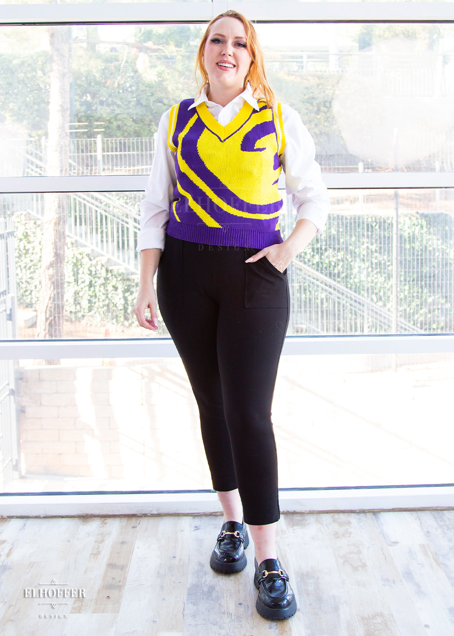 Kelsey, a size small fair skinned model with long ginger hair, is wearing a pullover vest with a boxy fit and v-neck. It is bright purple with a yellow swirl detail across the body.