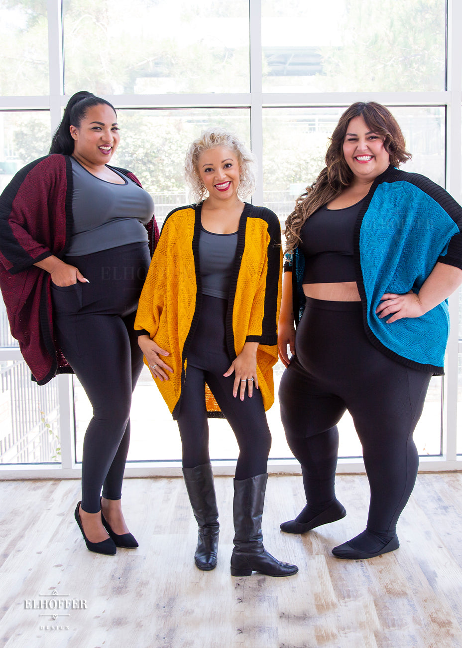 A photo of three models of various sizes wearing the three colors of the dolman; teal, yellow, and red.