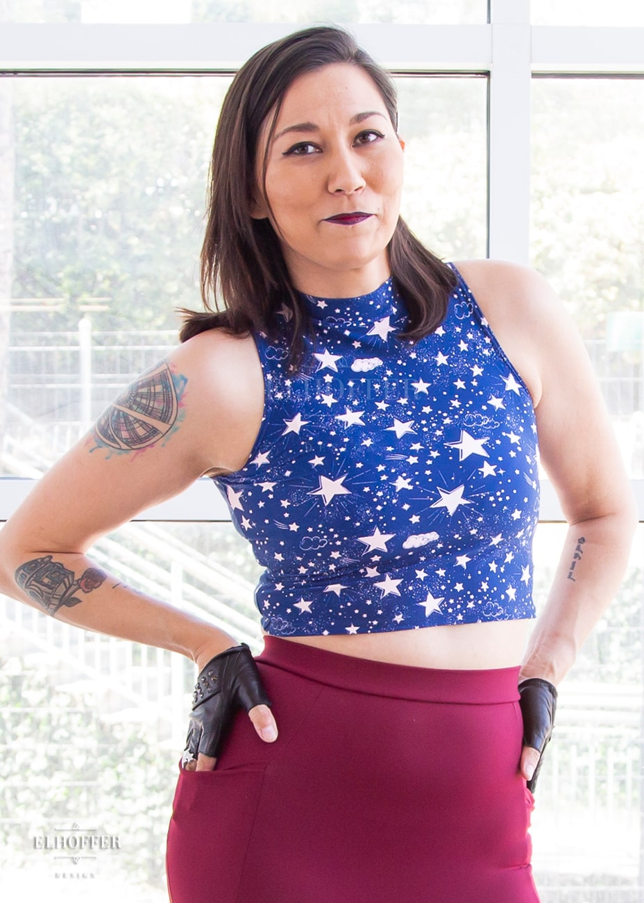 Susan, an olive skinned size XS model with short brown hair, wearing a mock turtle necked fitted sleeveless crop top ending at her waist in the queen of the night print. Queen of the night print is blue with light pink starts and clouds.