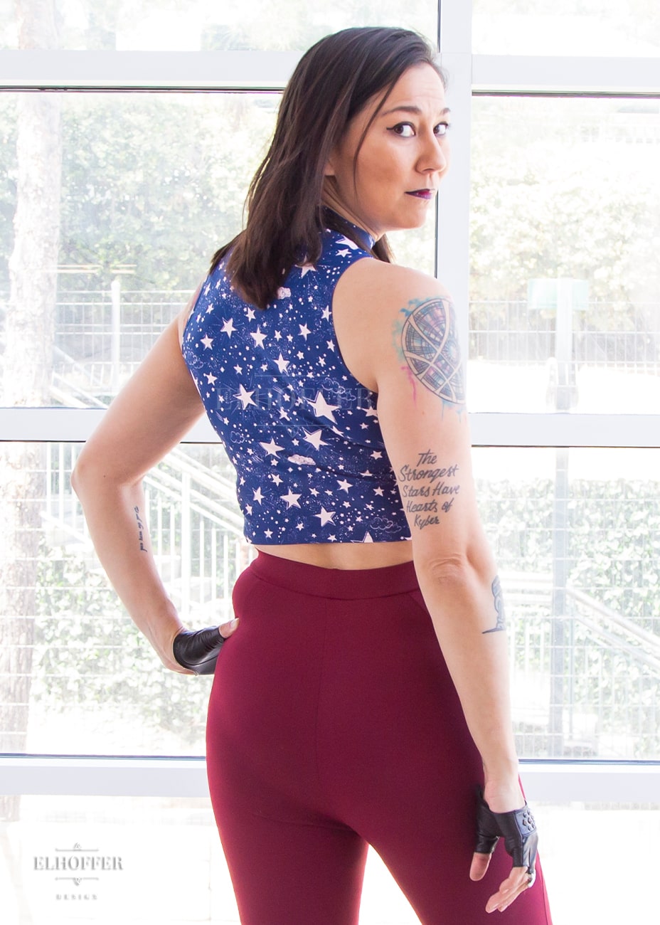Susan, an olive skinned size XS model with short brown hair, wearing a mock turtle necked fitted sleeveless crop top ending at her waist in the queen of the night print. Queen of the night print is blue with light pink starts and clouds. She has paired it with our burgundy Gwen leggings.