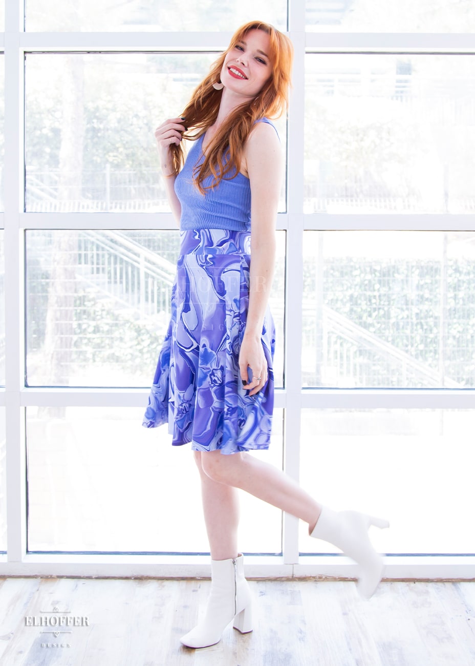 Chloe, a fair skinned size XS model with red hair and bangs, wears a high-waisted knee length full skirt with a fitted matching waistband encased with elastic in our periwinkle marble print. The periwinkle marble print is a marbled blue, purple, and white pattern all over it.