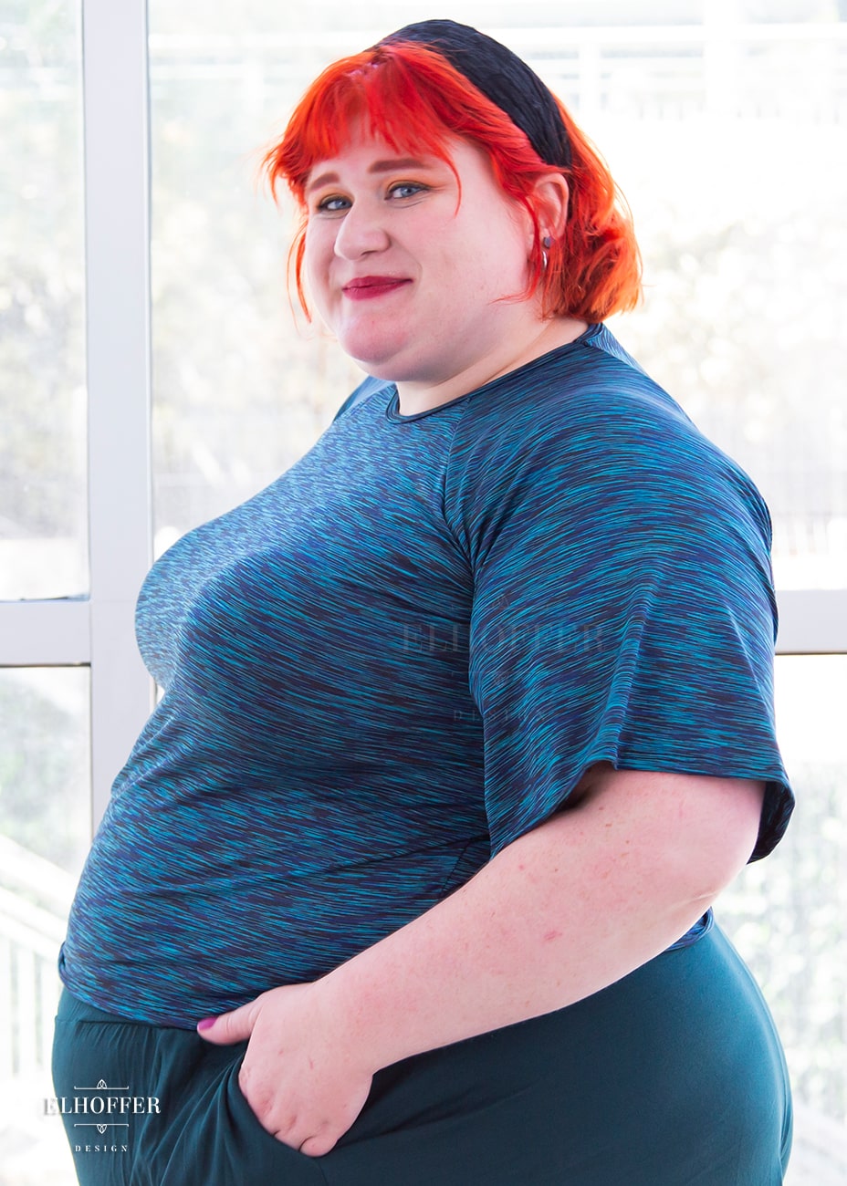 Logan, a fair skinned size 3XL model with short bright orange hair and bangs, is wearing a pullover gathered raglan sleeve top with short bell sleeves, in a heathered blue.