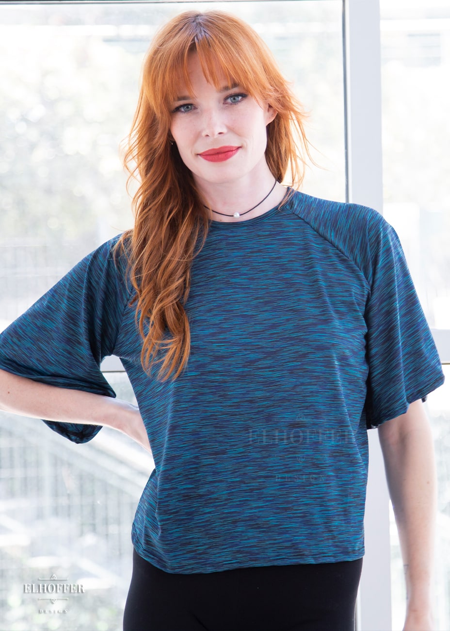 Chloe, a fair skinned size XS model with red hair and bangs, is wearing a pullover gathered raglan sleeve top with short bell sleeves, in a heathered blue.