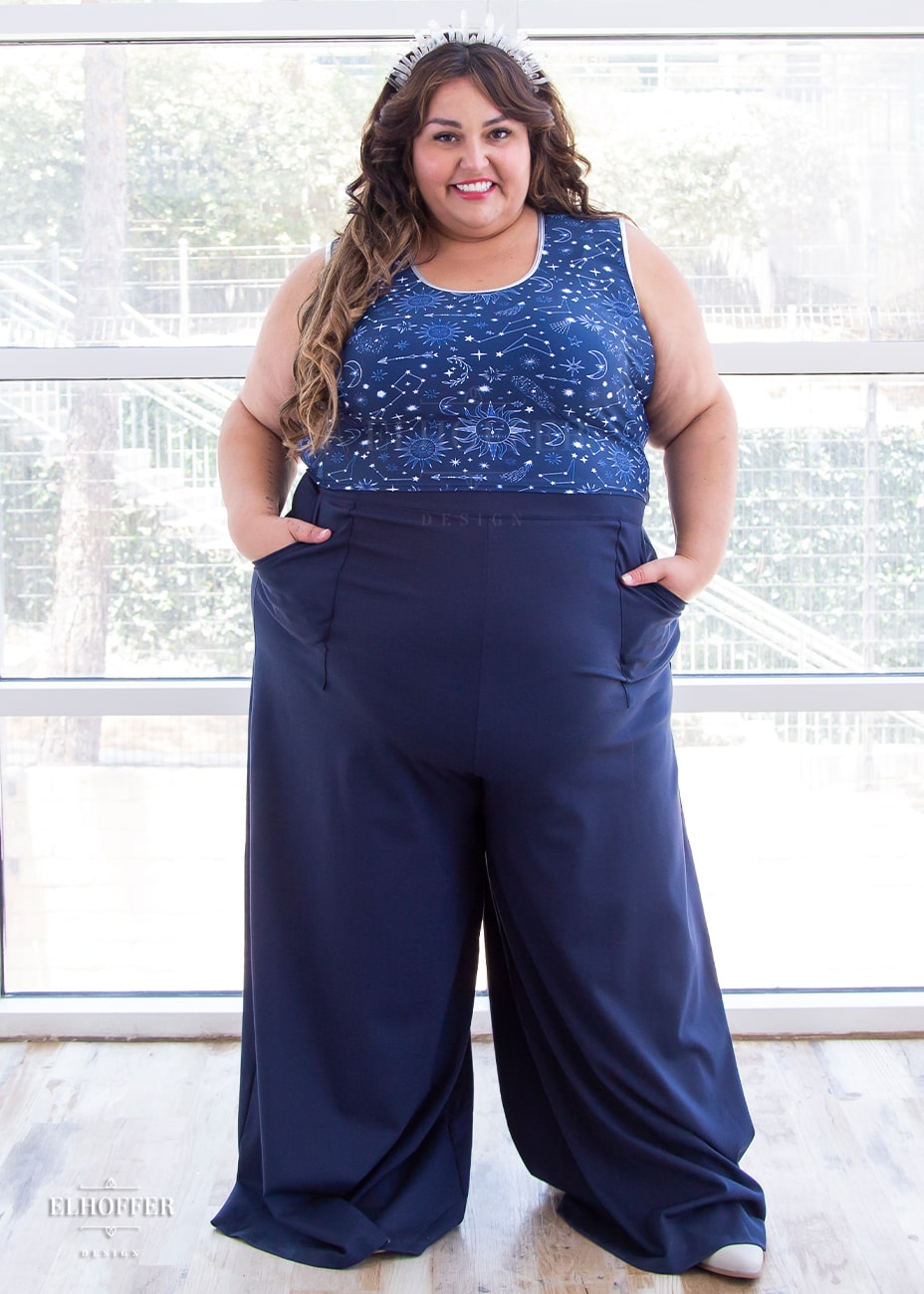 Kristen, a size 3XL olive skinned model with long brown highlighted hair is wearing high waisted full palazzo pants with front pockets and an invisible zipper on the side seam in navy.