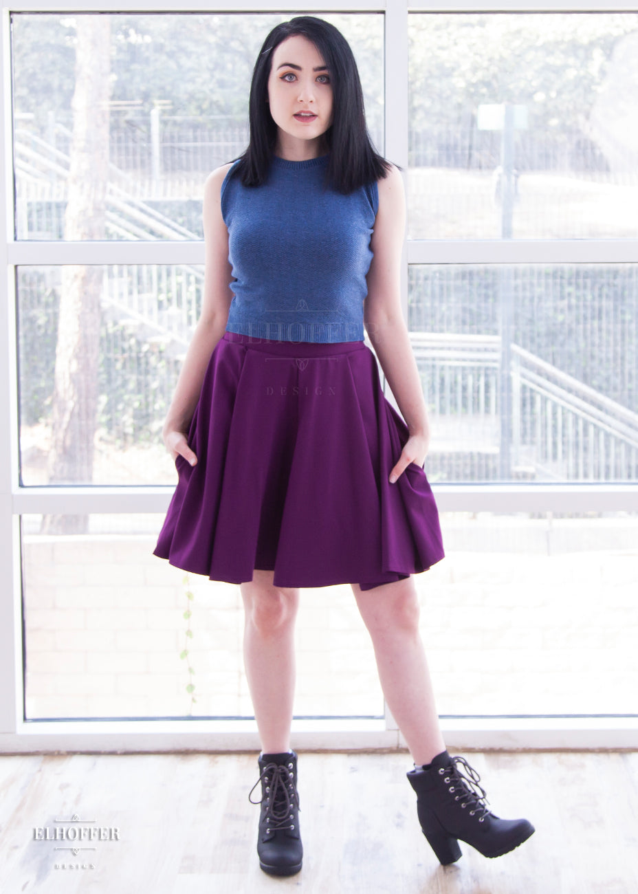 Amy (a fair skinned size medium model with short dark hair) models the knee length pleated plum purple skirt with pockets. She pairs it with a denim blue sleeveless knit Susan crop top.