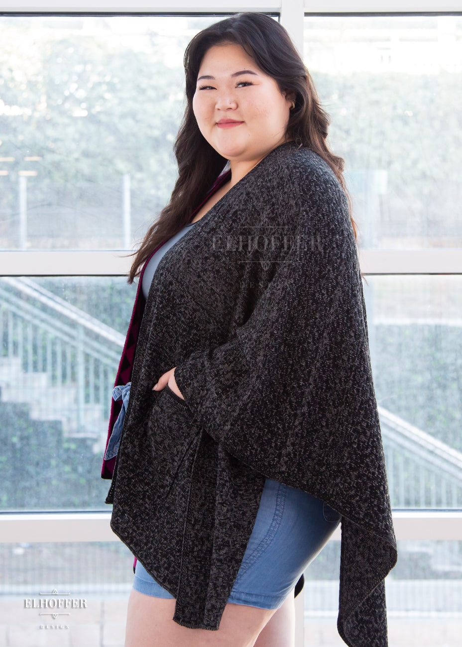 Ashley, an olive skinned XL model with long brown hair is wearing our open front poncho. One side is black triangles and pink triangles while the other is a heathered black.