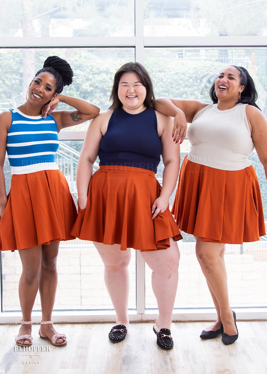 Krystina, Ashley, and Tas model the rust orange skater skirt paired with different high neck, sleeveless crop tops.