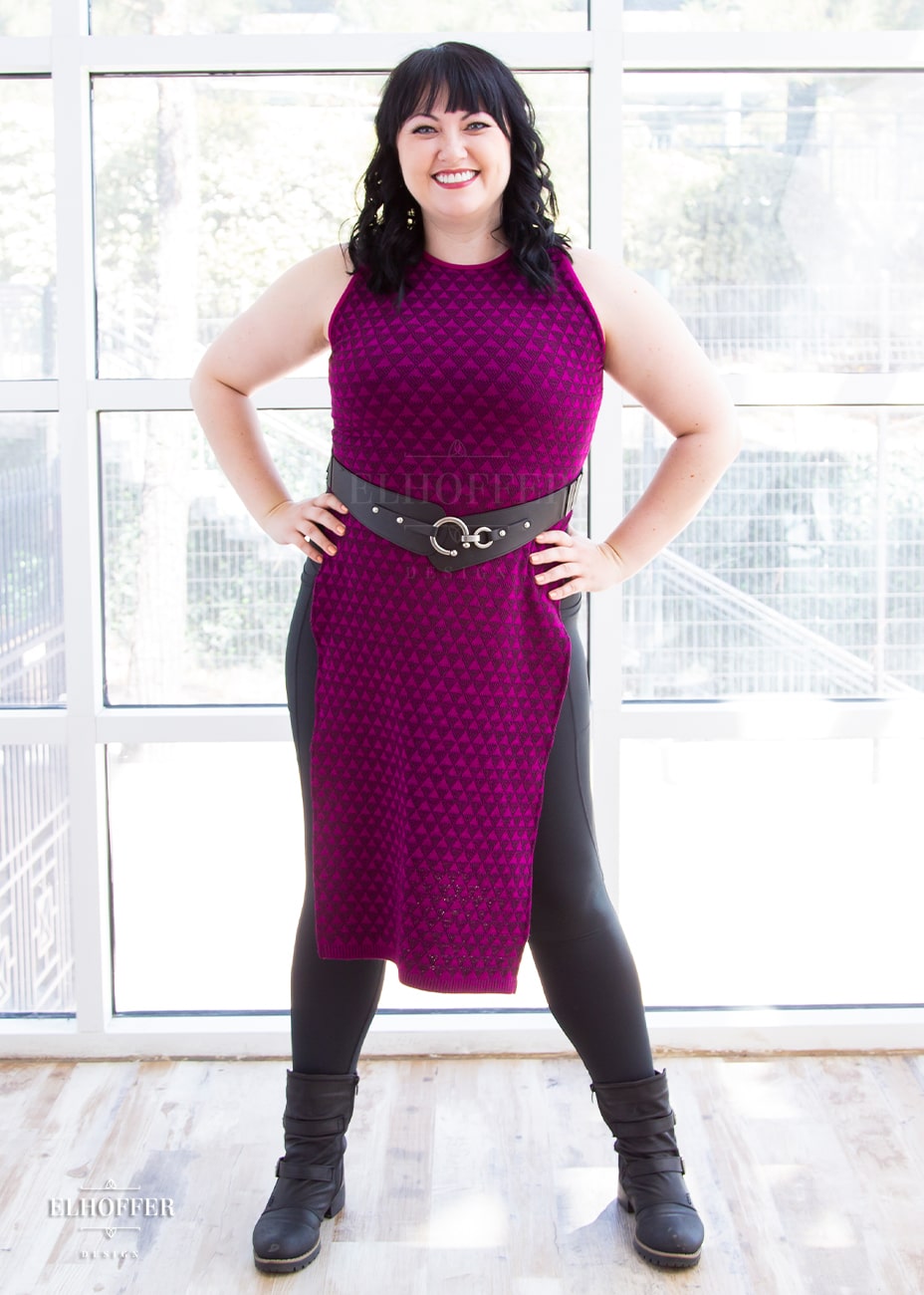 Bernadette, a fair skinned size large model with short black hair and bangs, is wearing a pullover cropped sleeveless knit top with front and back flaps in a magenta triangle knit.
